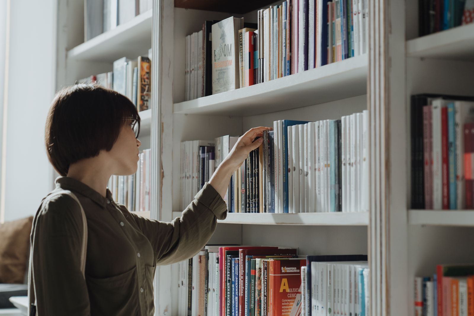 A woman standing at a bright bookshelf pulling out a book