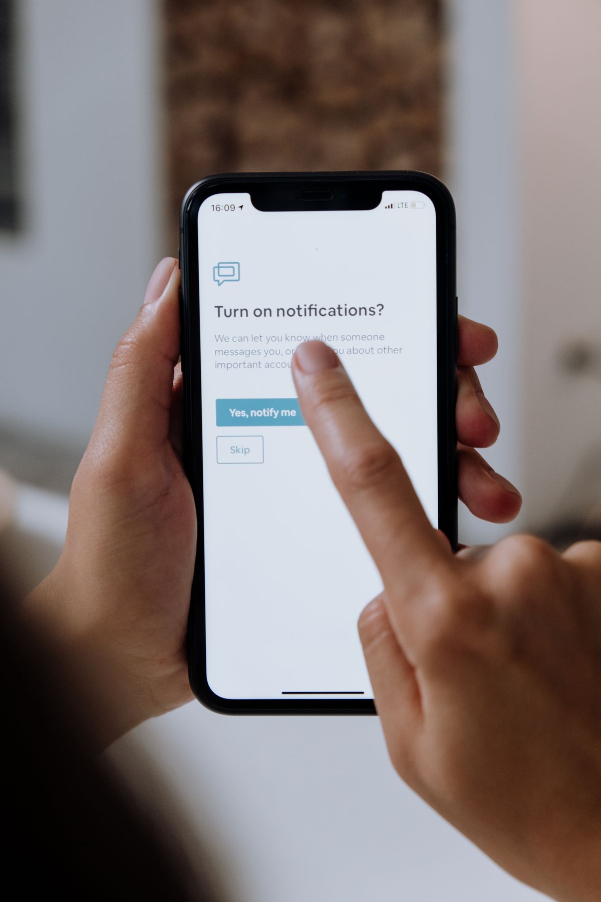 A hand holding a smartphone showing an app asking for permission to send notifications