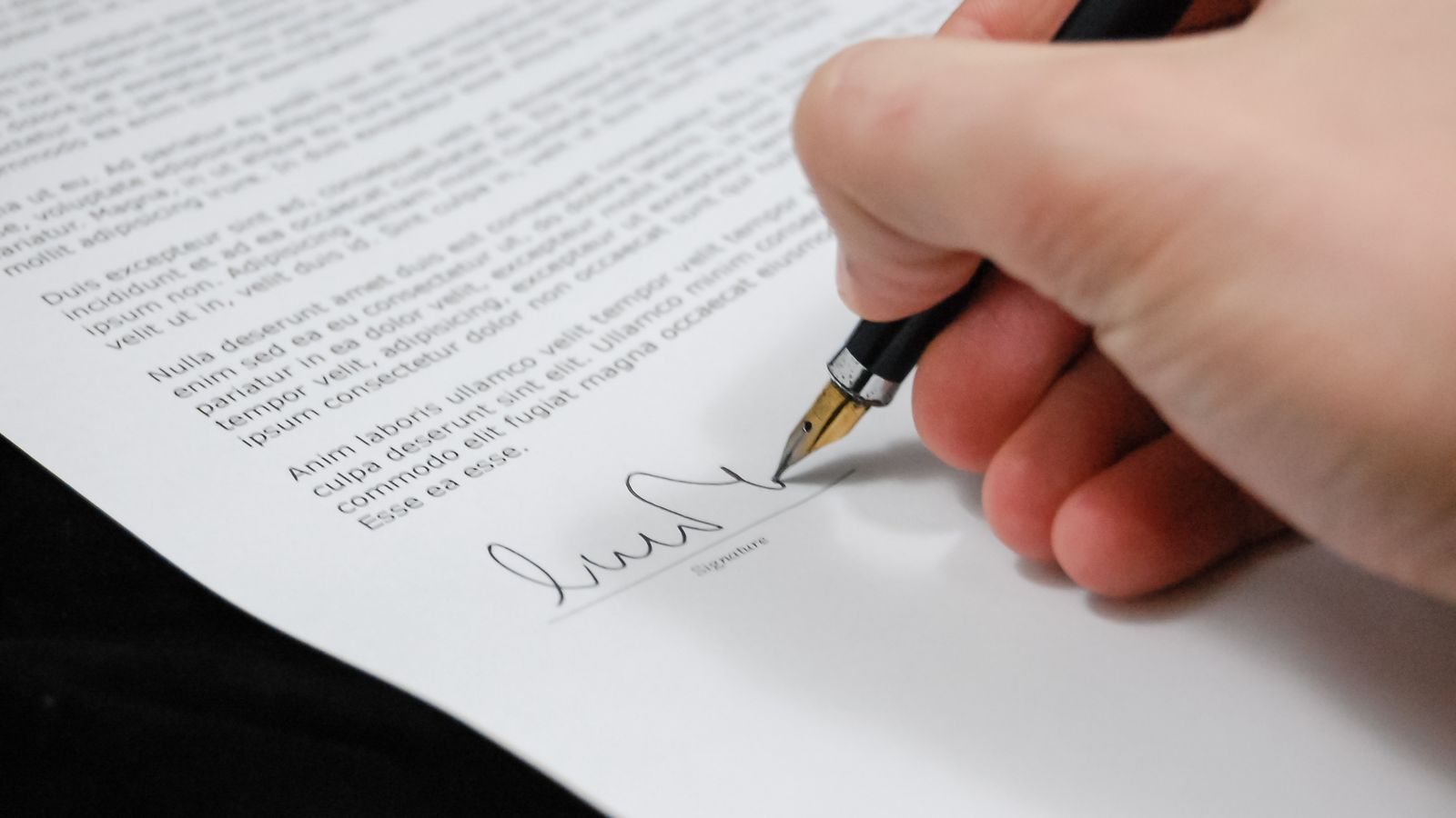 A hand signing a document with a fountain pen