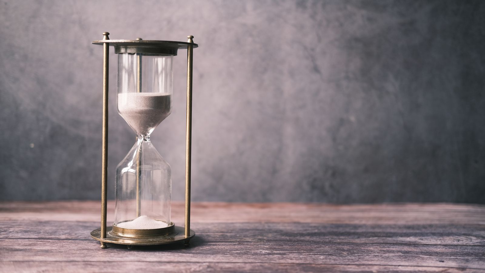 A brass-framed hourglass standing on a wooden table