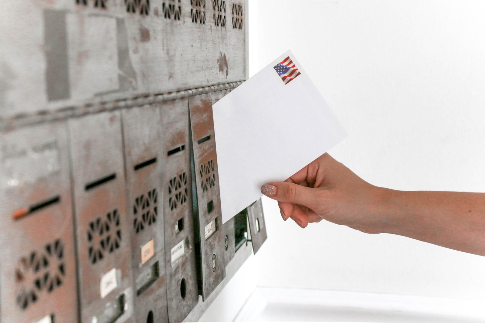 Eine Hand steckt einen weißen Briefumschlag in einen Briefkasten