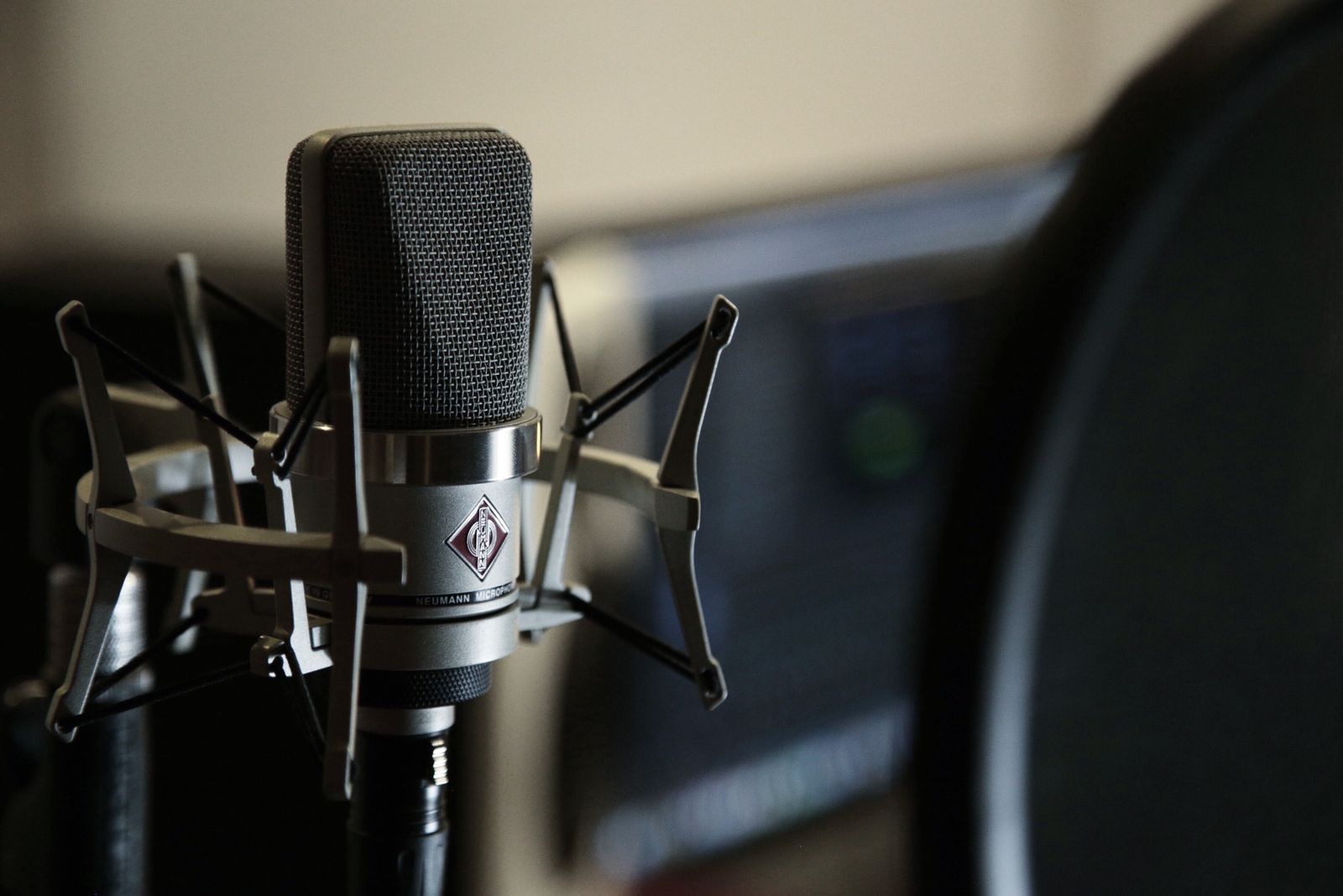 A silver studio microphone in a shock mount, a screen in the background
